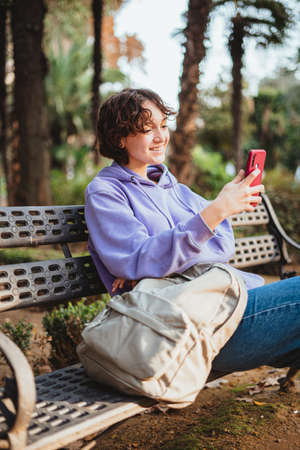 Girl sitting on a bench in a park video calling a friend.の写真素材