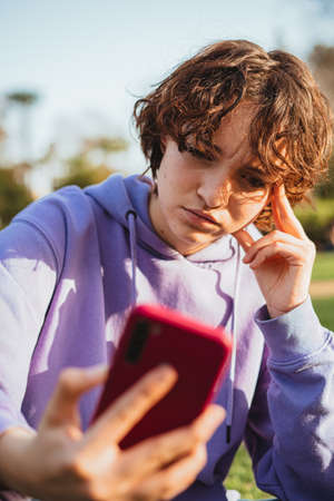 Girl wearing a purple hoodie is angry while looking at her phone in the park.の写真素材