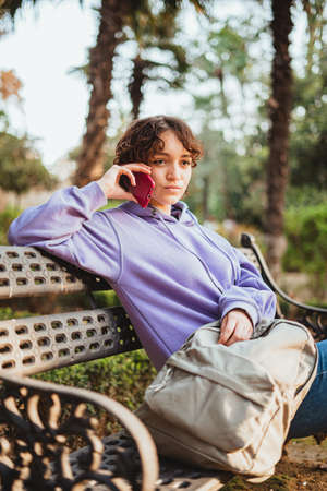 Teen girl sitting on a bench of a park talking with a friend on the phone.の写真素材