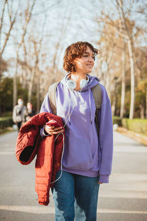 Student girl walking in a park with a school bag. She is holding her jacket.の写真素材
