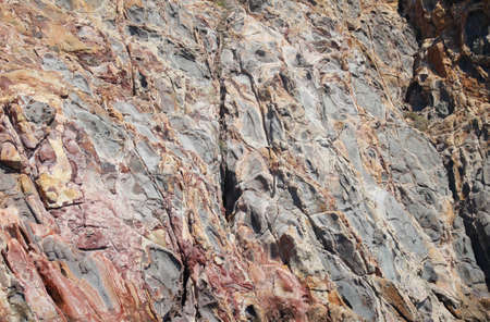 red, orange, white, yellow and black cliff rock texture on the island of milosの写真素材