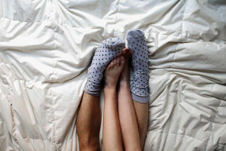couples feet together with fluffy socks on bedの写真素材