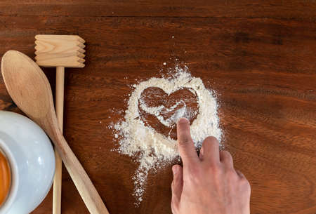 Heart shape with flour on rustic wooden countertop background and natural wood kitchen utensilsの写真素材