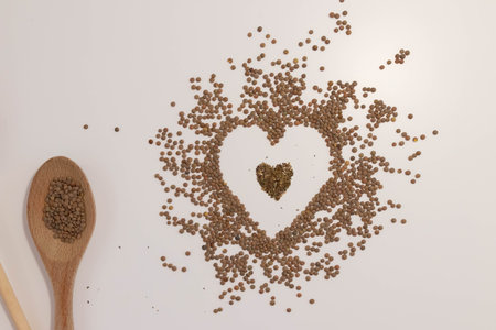 Heart made of raw lentils on a white background with kitchen utensilsの写真素材