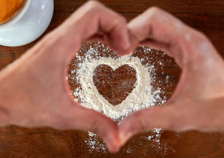 Heart shape with flour on rustic wooden countertop background and natural wood kitchen utensils