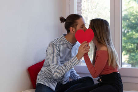 Couple in love kissing behind a red heartの写真素材