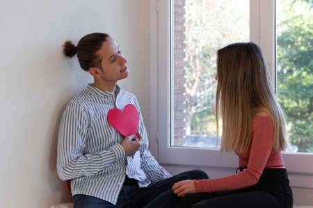 Couple in love sitting at a window with a red heartの写真素材