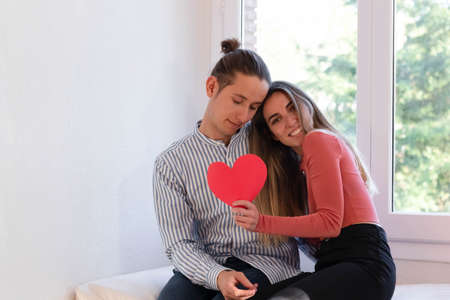 Couple in love hugging each other while holding a red heartの写真素材