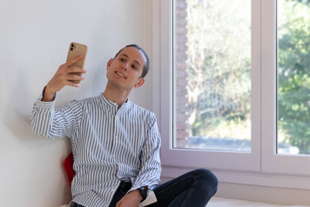 Young man sitting taking a selfie and smilingの写真素材