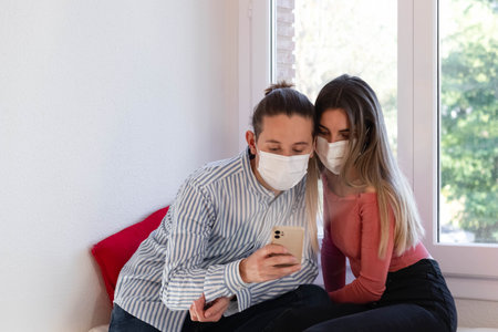 Man and woman wearing a face mask looking at the smartphoneの写真素材