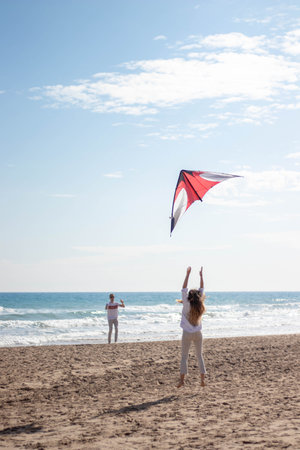 young couple holding and jumping a kite and playing on the beachの写真素材