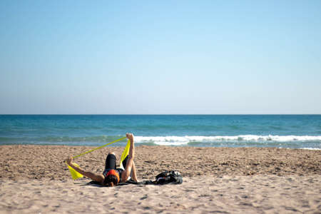 Adult woman exercising with rubber bands on the beach lying down on the beachの写真素材