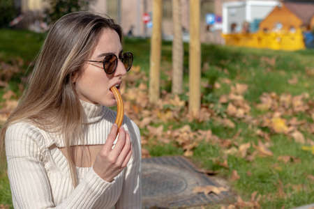 Young girl in winter outfit eating churros at a Christmas marketの写真素材