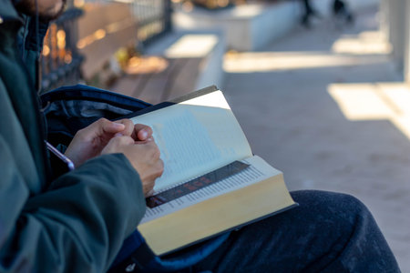 Young man reading a book sitting on a bench in a parkの写真素材