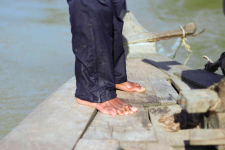 feet of poor barefoot fisherman in blue pants in old wooden canoe in cambodiaの写真素材