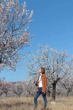 Young photographer enjoying the sunny day in a field of almond blossoms field in spring under blue skyの写真素材
