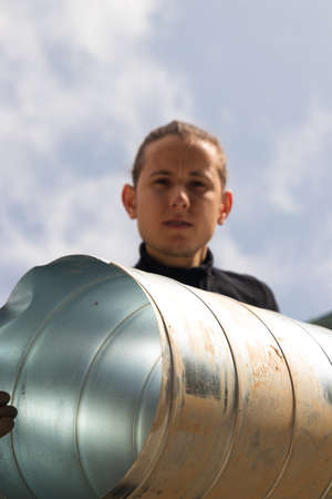 Low angle view of a young working man holding a metal or aluminium ductの写真素材