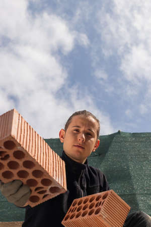 Low angel view of young labourer holding some bricks in a blue sky backgroundの写真素材