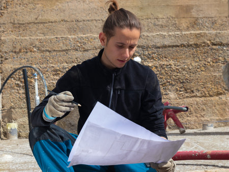 Young man working and running a construction site holding the blueprintsの写真素材