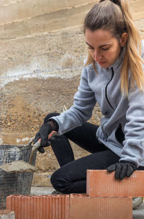 Young woman building a brick wall by pouring cement to join the pieces togetherの写真素材