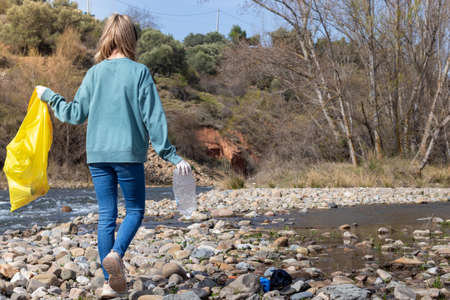 Woman backwards walking the riverbank looking for garbageの写真素材