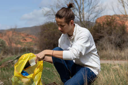 Young man frustrated by all the garbage found in the field as he stuffs a bottleの写真素材