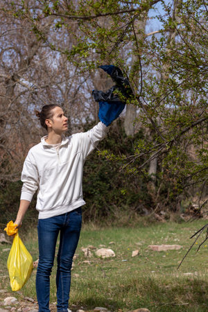 Man with a raised hand picking up garbage bag hooked on windblown treeの写真素材
