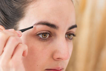 Close up portrait of young caucasian woman tweezing her eyebrowsの写真素材