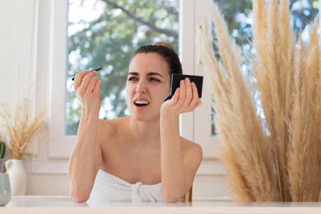 Woman with a gesture of pain plucking her eyebrows with a towel on her body