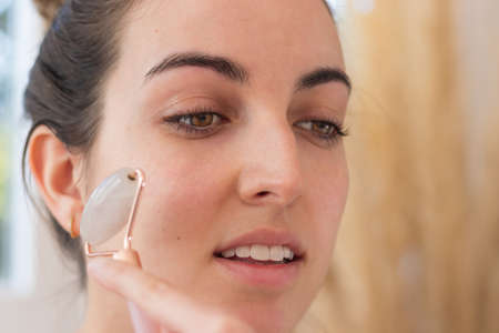 Smiling woman using face roller on her cheek while doing her beauty routineの写真素材