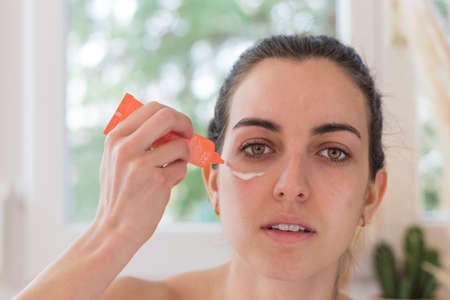 Young woman applying eye cream on her perfect fresh skin at home beauty routineの写真素材