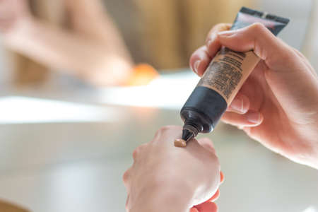 Woman pouring foundation on her hand as color swatch before doing make up