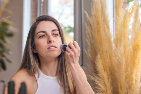 Portrait of young woman applying make up foundation on her face with brushの写真素材