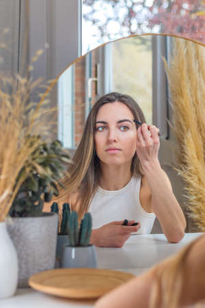 Beautiful woman painting her eyebrows while putting on makeup in her vanityの写真素材