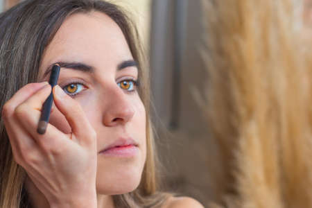 Close up view of yellow and honey eyes woman painting her eyebrows doing makeup