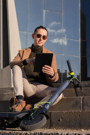 Vertical smiling young man using a table sitting in the financial district commuting with and electric scooterの写真素材