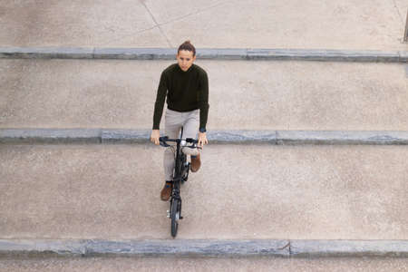 Overhead shot of young man riding a bicycle going down the stair of his work office building in the financial districtの写真素材