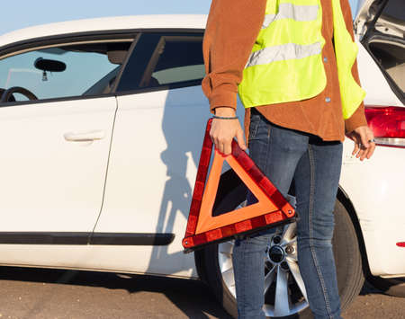 unrecognizable man holding a red triangle on the road with broken car and breakdown conceptの写真素材