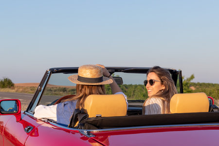 Side view of beautiful young women talking, smiling and having fun driving around the country on a...