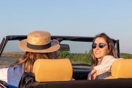 Close up of two young women driving a convertible car while looking at camera on a sunny and blue summer dayの写真素材