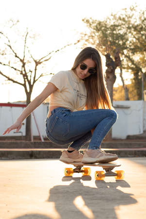 Backlit photography of an amazing young teenage girl rolling her longboard in a sporty wayの写真素材