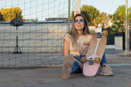 Portrait at sunset of a girl resting after a day of skateboarding laughing and looking at the light