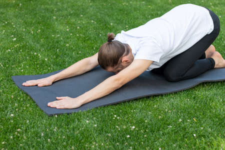 Young hipster unrecognizable man bended on the floor stretching on a yoga mat after exercising in the gardenの写真素材