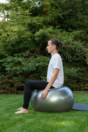 Vertical view of young fit man stright sitting on a balance ball to gain stability practising yoga in the outside gardenの写真素材