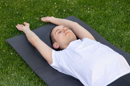 Young man stretching himshelf on a yoga black mat with arms outstretched. Eyes closed and breathing...