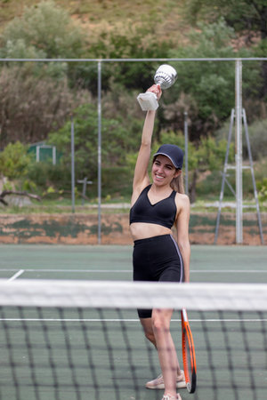 Young amateur tennis player woman happy smiling raising her arm holding a cup as a sign of victoryの写真素材