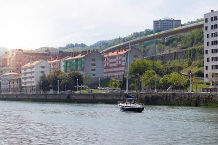 BILBAO, SPAIN-MAY, 5TH, 2022: Sunny spring day city scape in Bilbao riverbank with a sailboat sailing throw the riverのeditorial素材