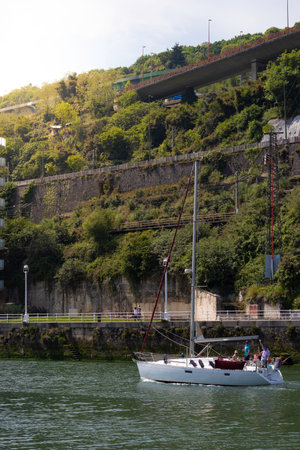 BILBAO, SPAIN-MAY, 5TH, 2022: Vertical view of sailboat sailing on the river of the European city and people wavingのeditorial素材