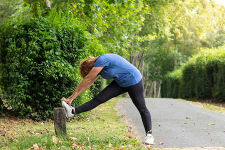 Mature female in activewear doing exercise for leg stretch while enjoying workout in natural...