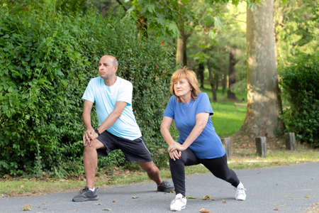 Mature men and woman stretching together as a couple in a city park green natural enviromentの写真素材